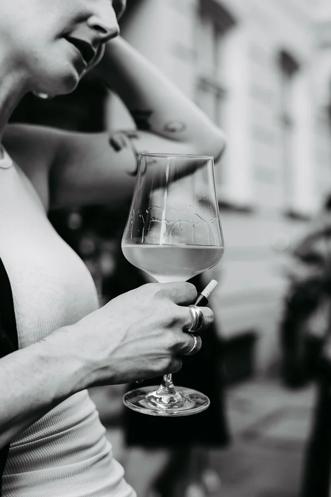 Frau hält ein Weinglas mit Wasser und Zigarette, im Hintergrund städtische Umgebung in Schwarz-Weiß