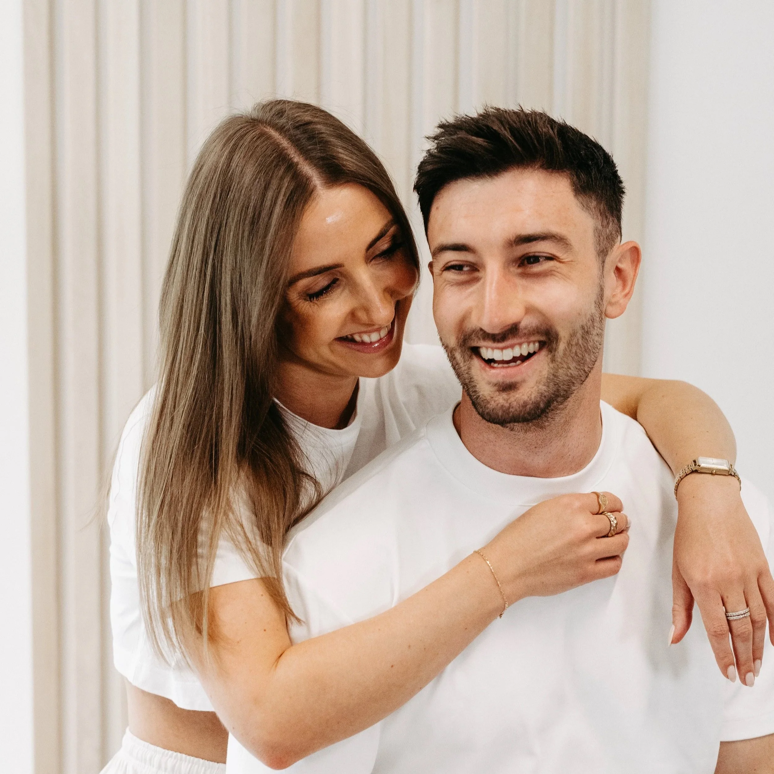 Lächelndes Paar, die Frau sitzt auf den Schultern des Mannes, umarmt ihn und lächelt liebevoll.