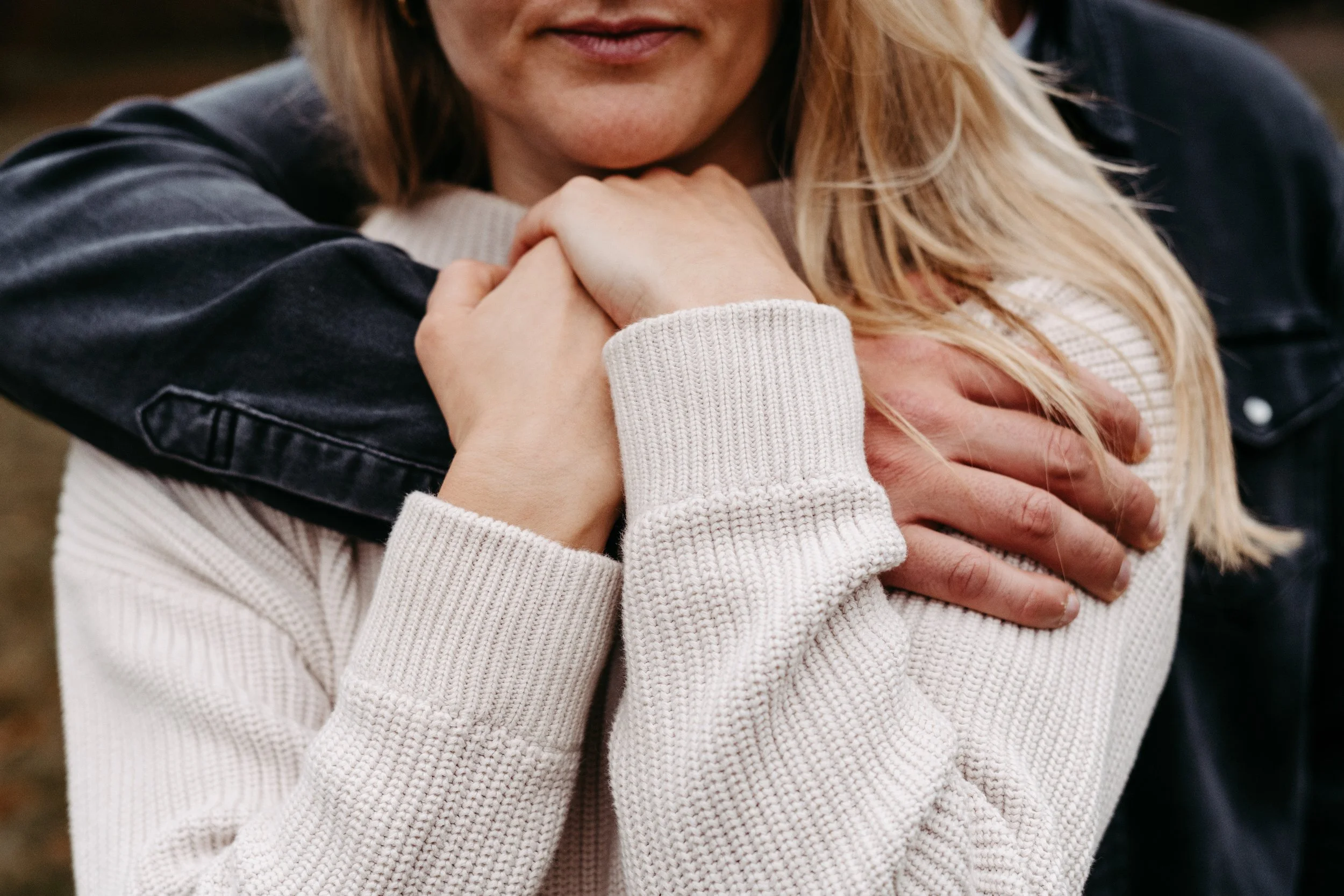 Zwei Frauen umarmen sich eng, eine trägt einen weißen Strickpullover und die andere eine dunkle Jacke. Die Szene ist herzlich und zeigt Nähe und Zuneigung.