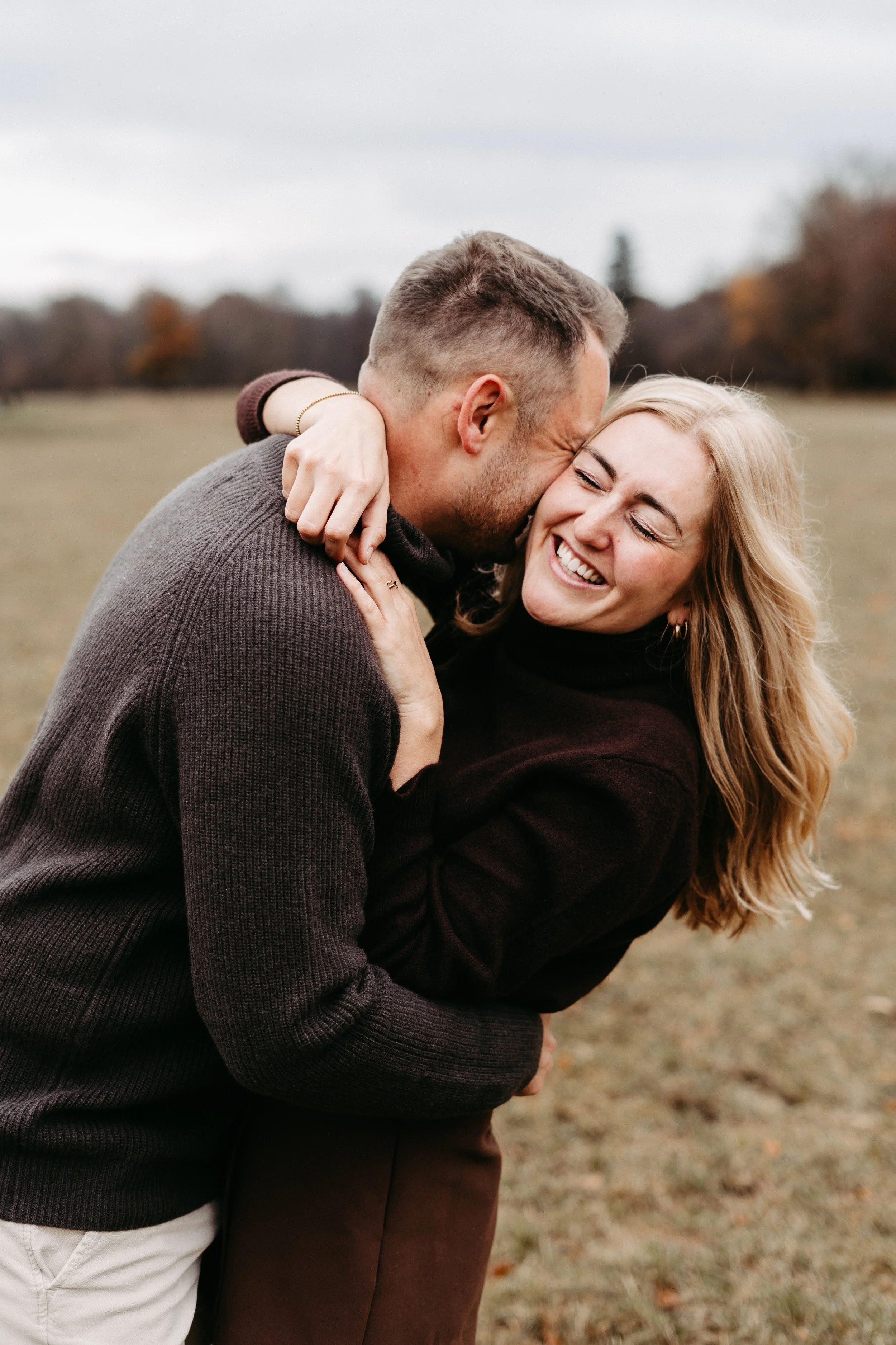Ein Paar umarmt sich lachend im Freien bei herbstlichem Wetter.