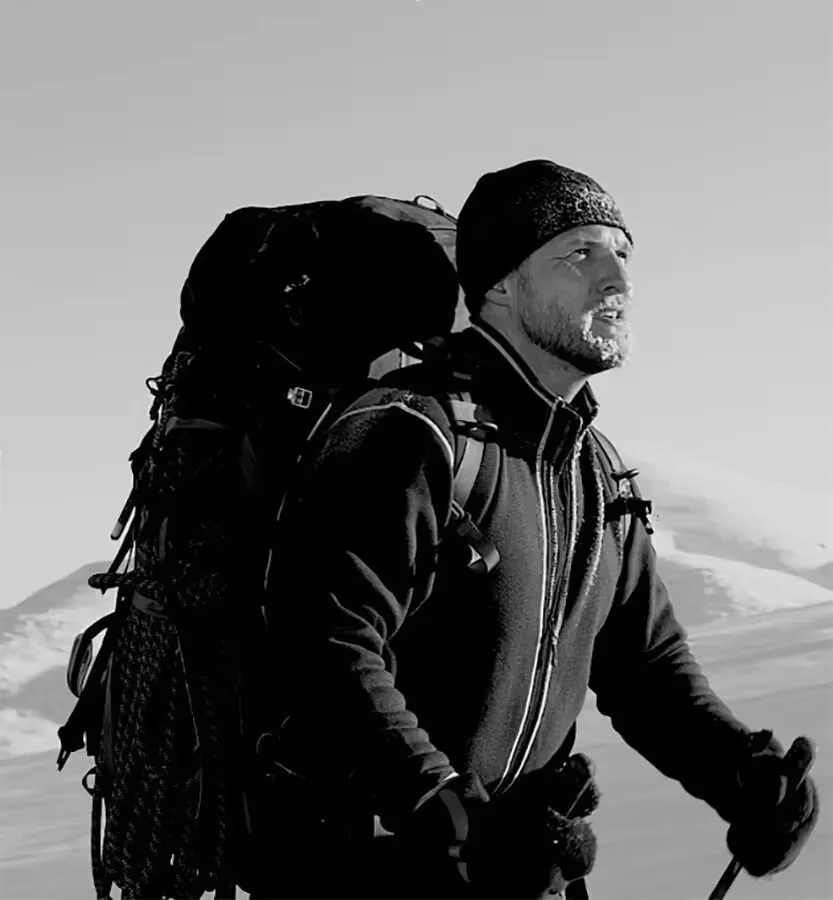 Man in winter gear with a backpack hiking outdoors in a snowy landscape.