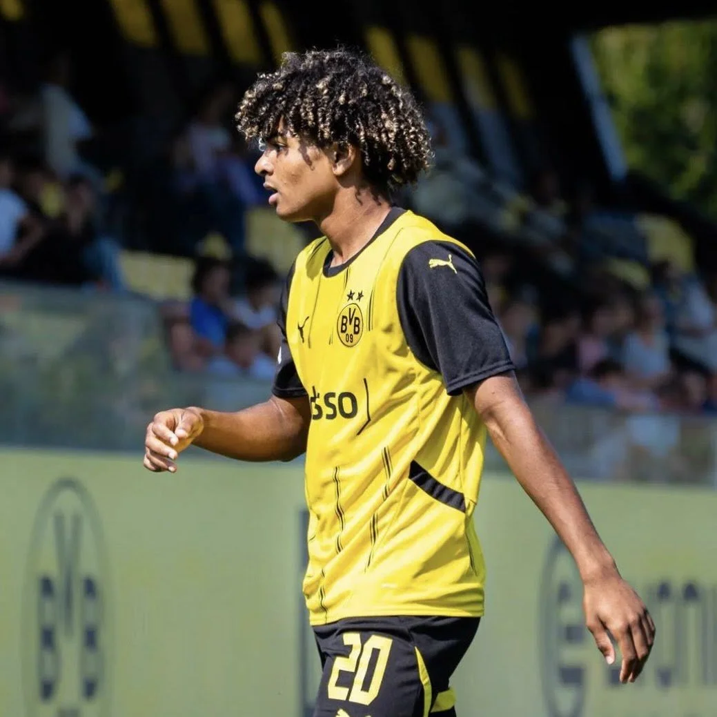 A soccer player with curly hair wearing a yellow and black Borussia Dortmund jersey during a match.