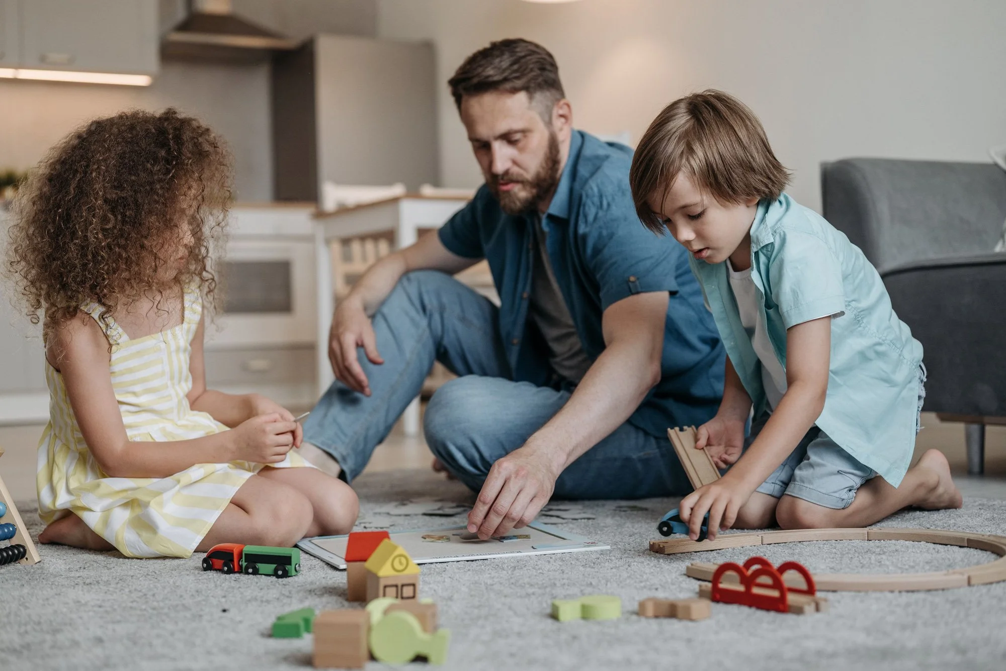 A man and two children playing with wooden toys on a carpeted floor in a living room practicing PCIT.