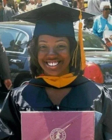 Woman in graduation cap and gown holding a diploma at an outdoor ceremony.