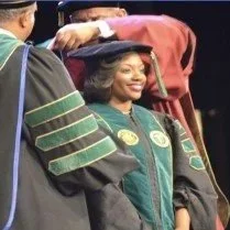 A young woman smiling in graduation gown and cap during a graduation ceremony.