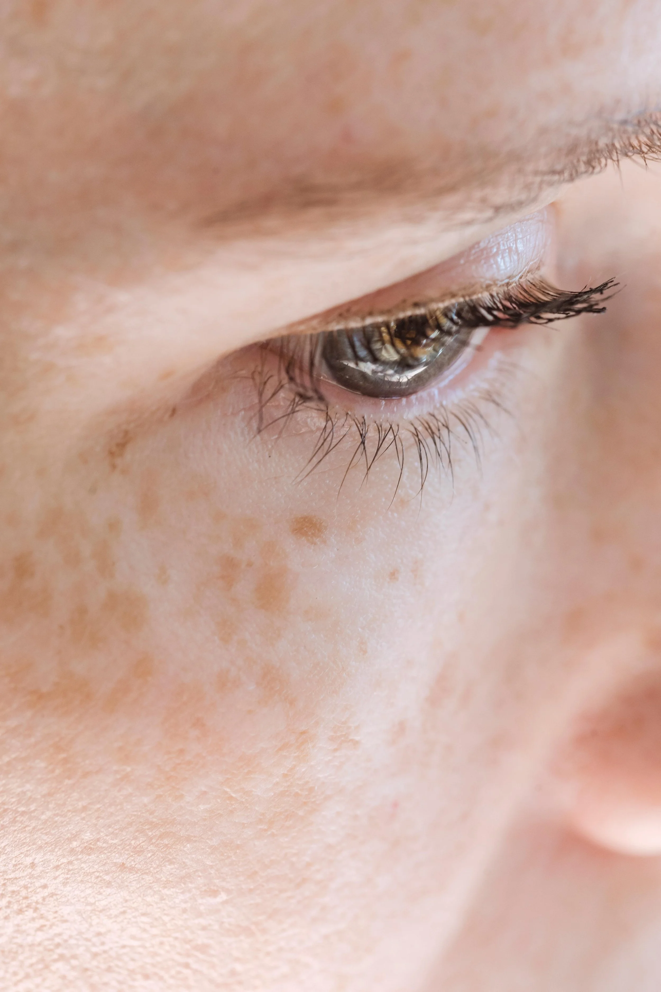Close-up of a person's face focusing on the eye, showing detailed eyelashes, brown iris, and freckles on the cheek.