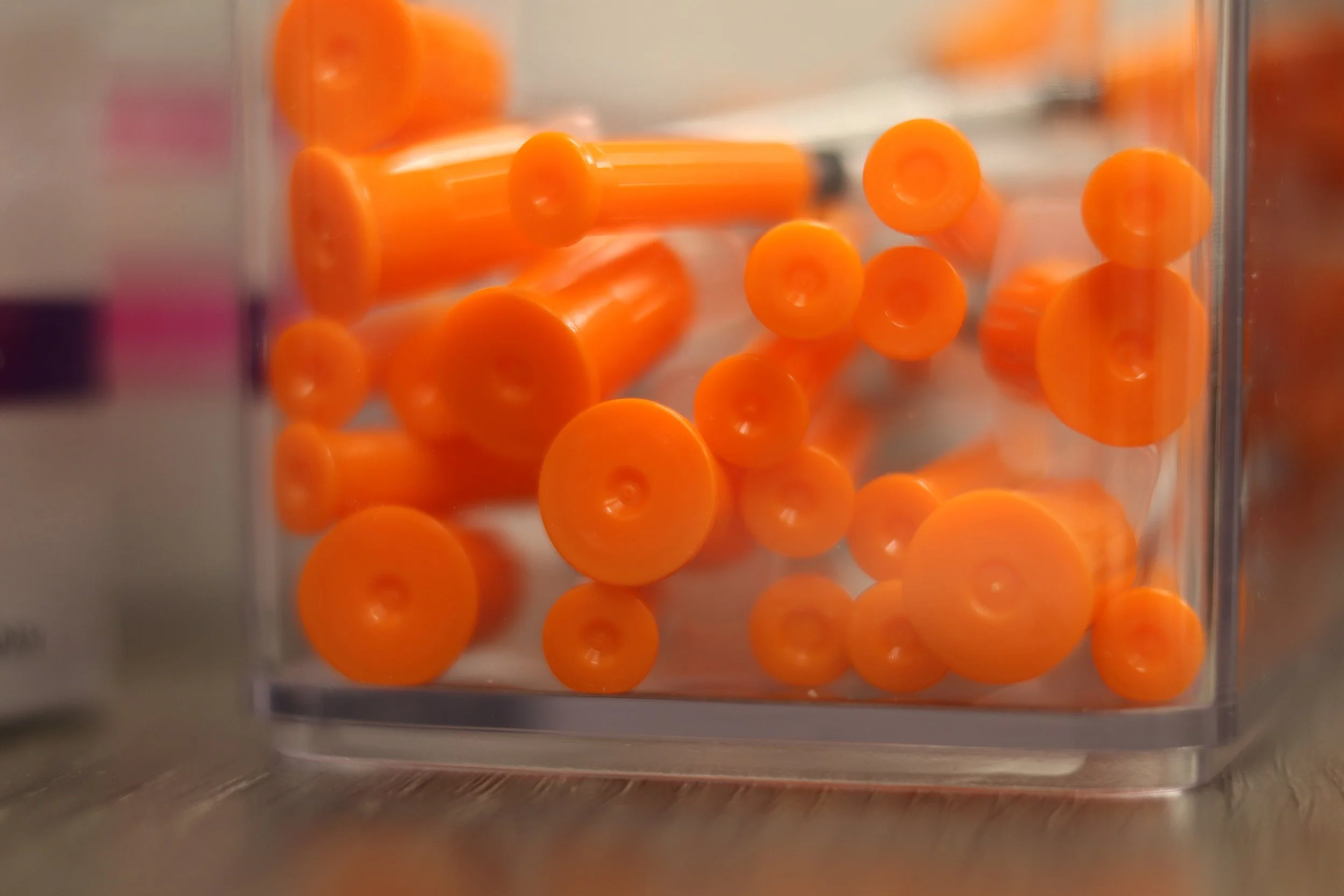 Orange plastic nail polish bottle caps inside a clear plastic container.