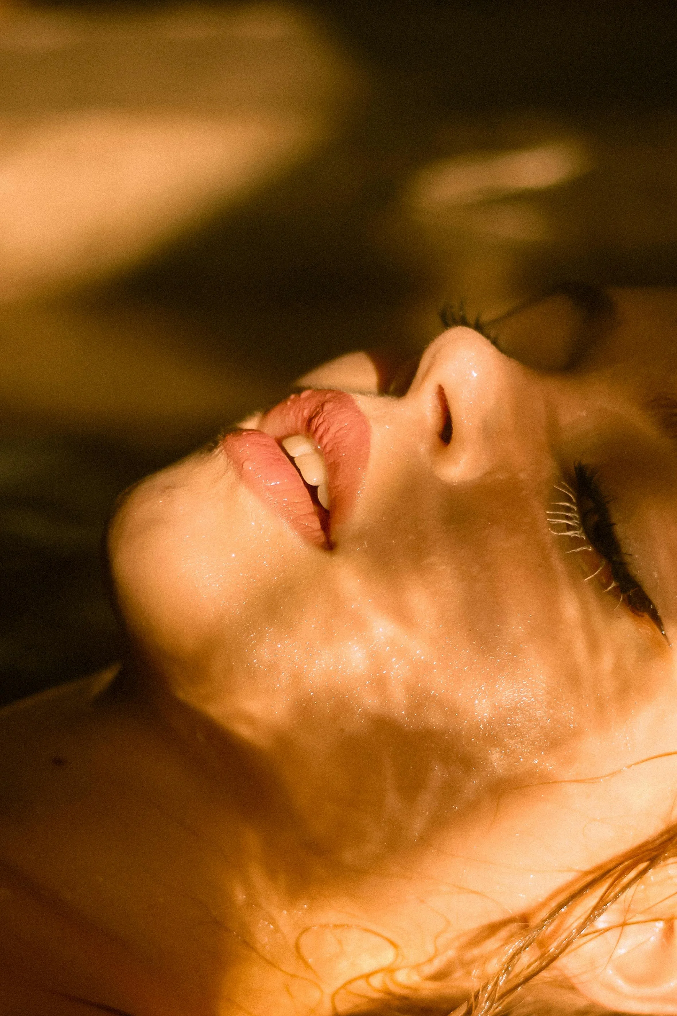 Close-up of a woman's face, tilting her head back with her eyes closed, showing her lips slightly parted and a hint of a smile.