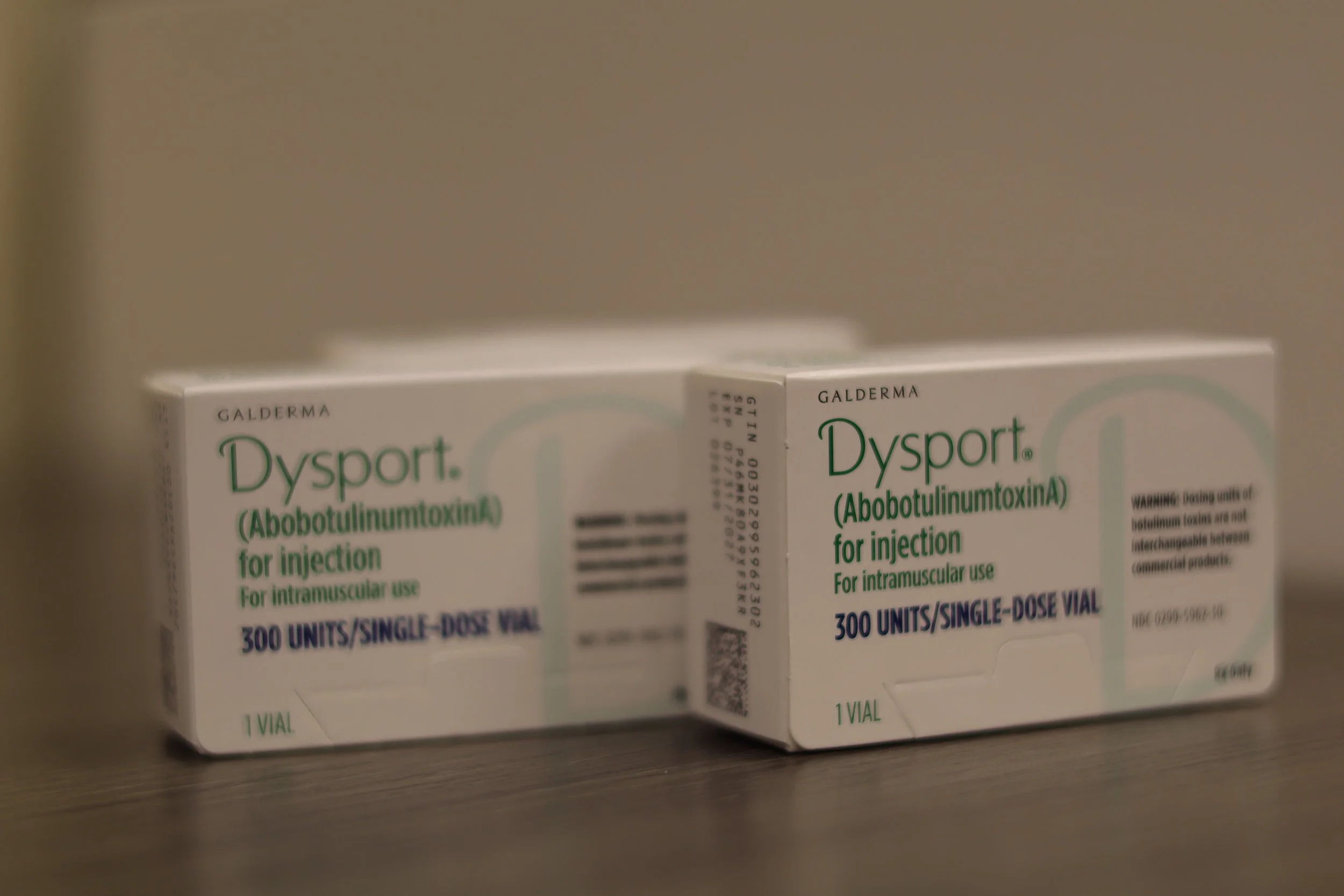 Two boxes of Dysport (AbobotulinumtoxinA) for injection, a medication used for intramuscular use, with each box containing 300 units in a single-dose vial, placed on a wooden surface.