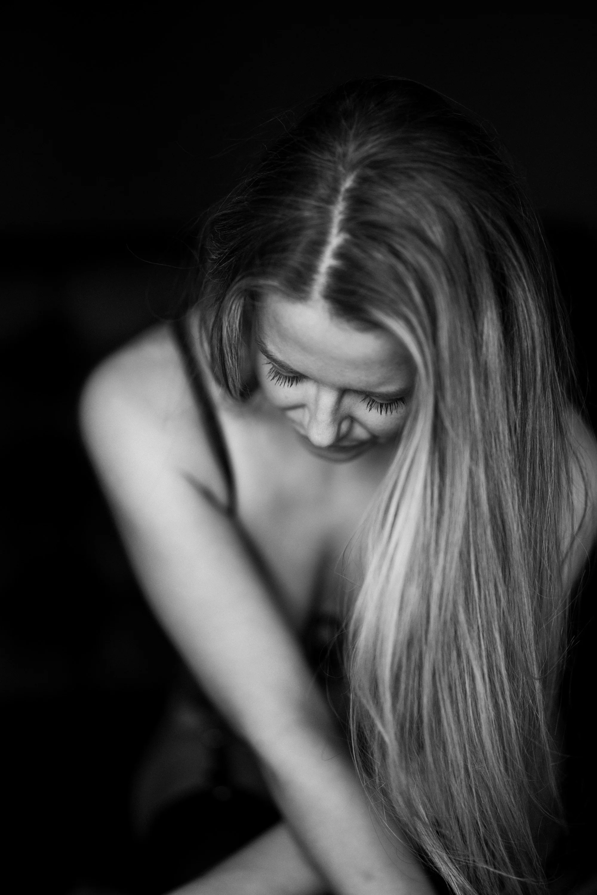 A black and white photo of a woman with long hair looking downward, with her eyes closed and a slight smile.