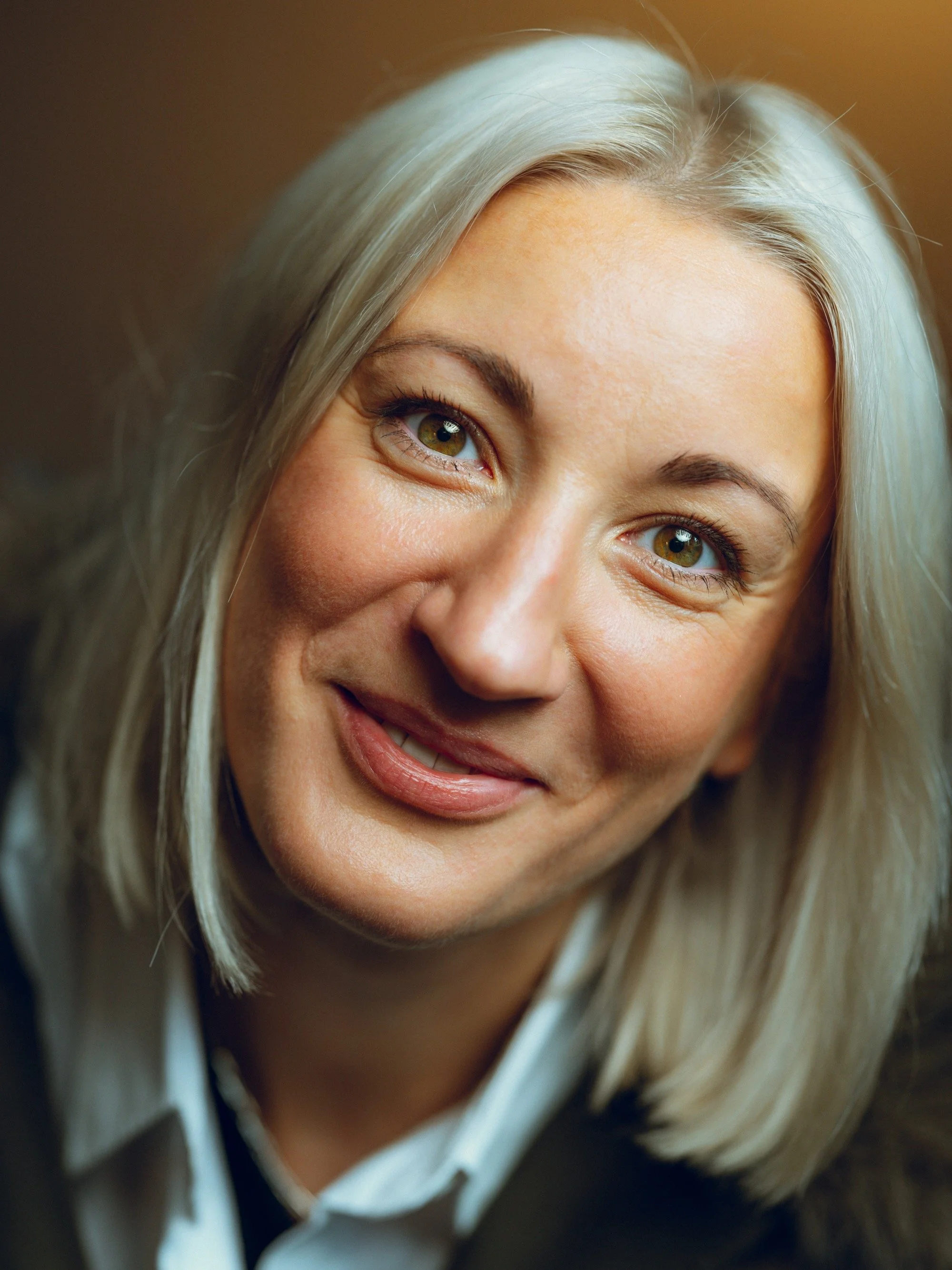Close-up of a smiling woman with blonde hair and hazel eyes.