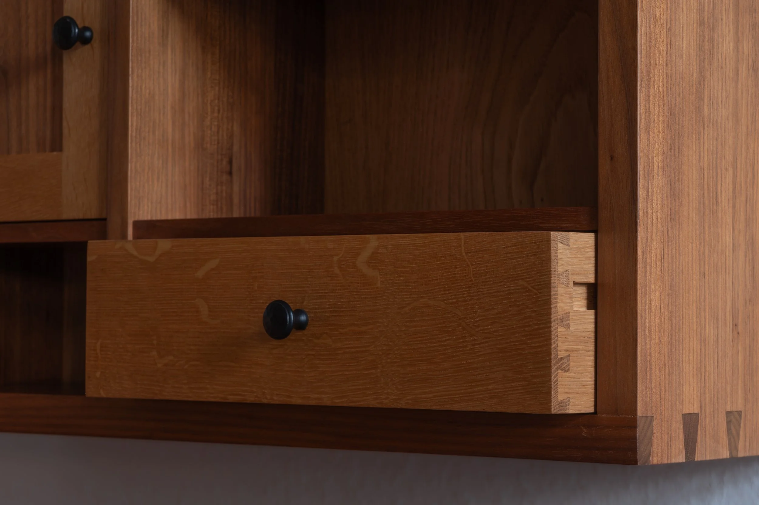 Detailaufnahme eines handgefertigten Hängeschranks aus Nussbaum und Eiche mit offenen Fächern, Tür und Schublade mit Schwalbenschwanzverbindung