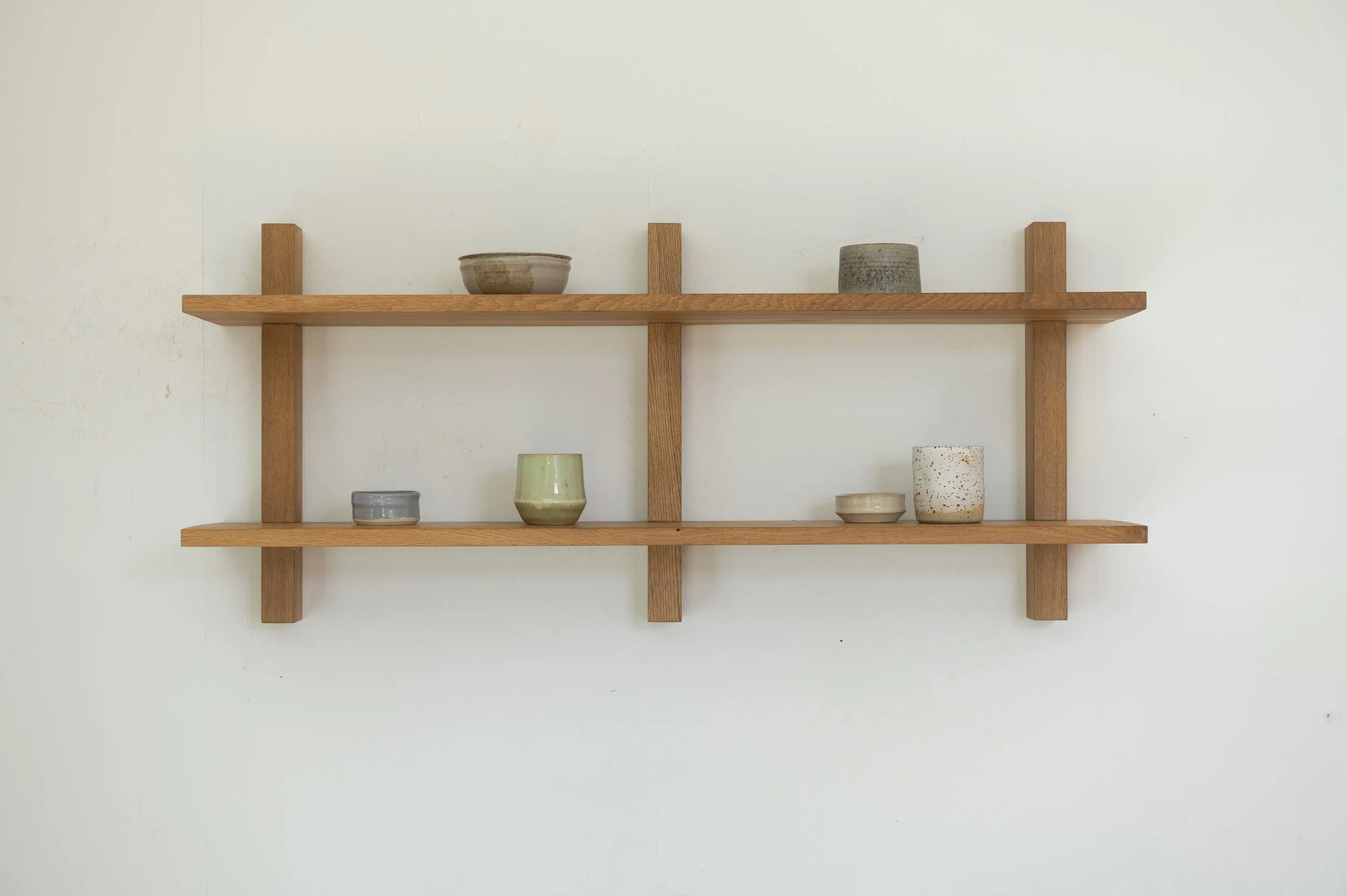 Steckregal aus Eiche an der Wand mit dekorativen Keramikobjekten in minimalistischer Anordnung