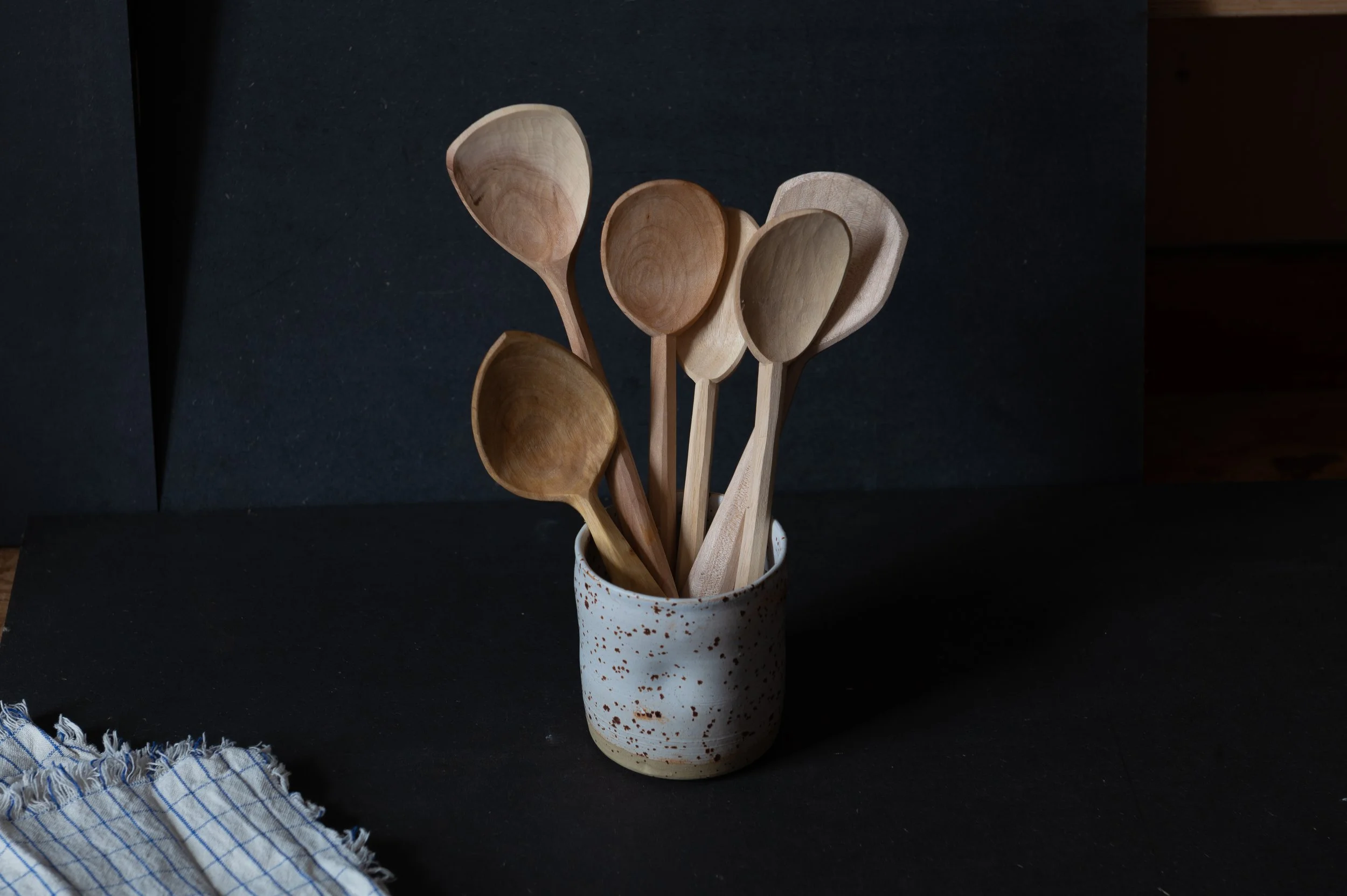 Auswahl an Holzlöffel in Keramiktasse vor schwarzem Hintergrund