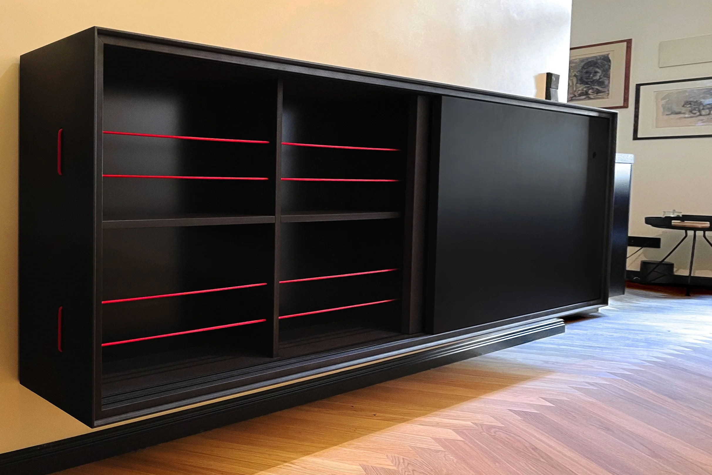 Wandhängendes Schuhregal aus schwarzem MDF mit geöffneten Schiebetüren, rote elastische Bänder als Schuhhalterung in den Fächern, auf Fischgrätparkett