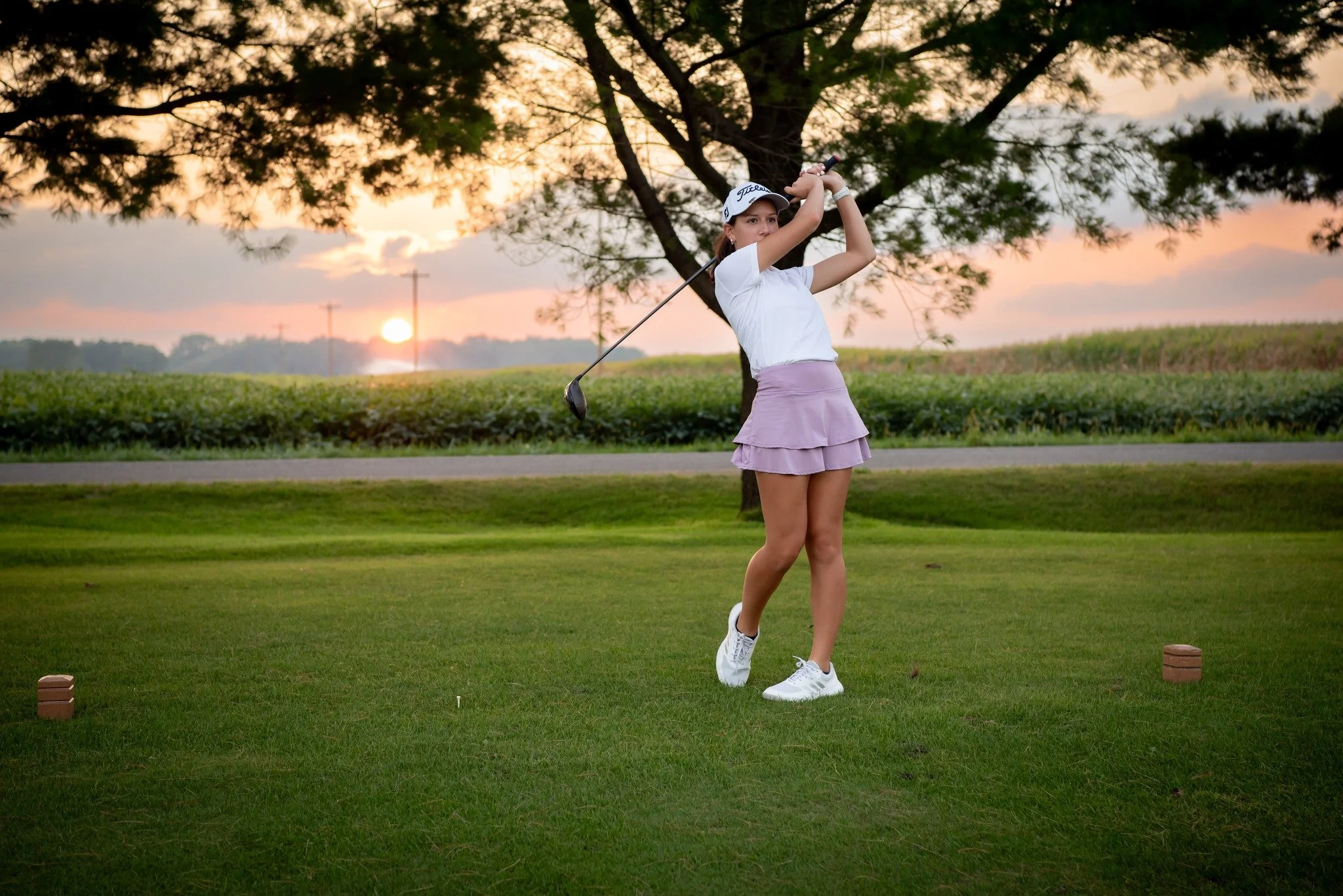 Young woman playing golf on a grassy course at sunset, swinging her club.
