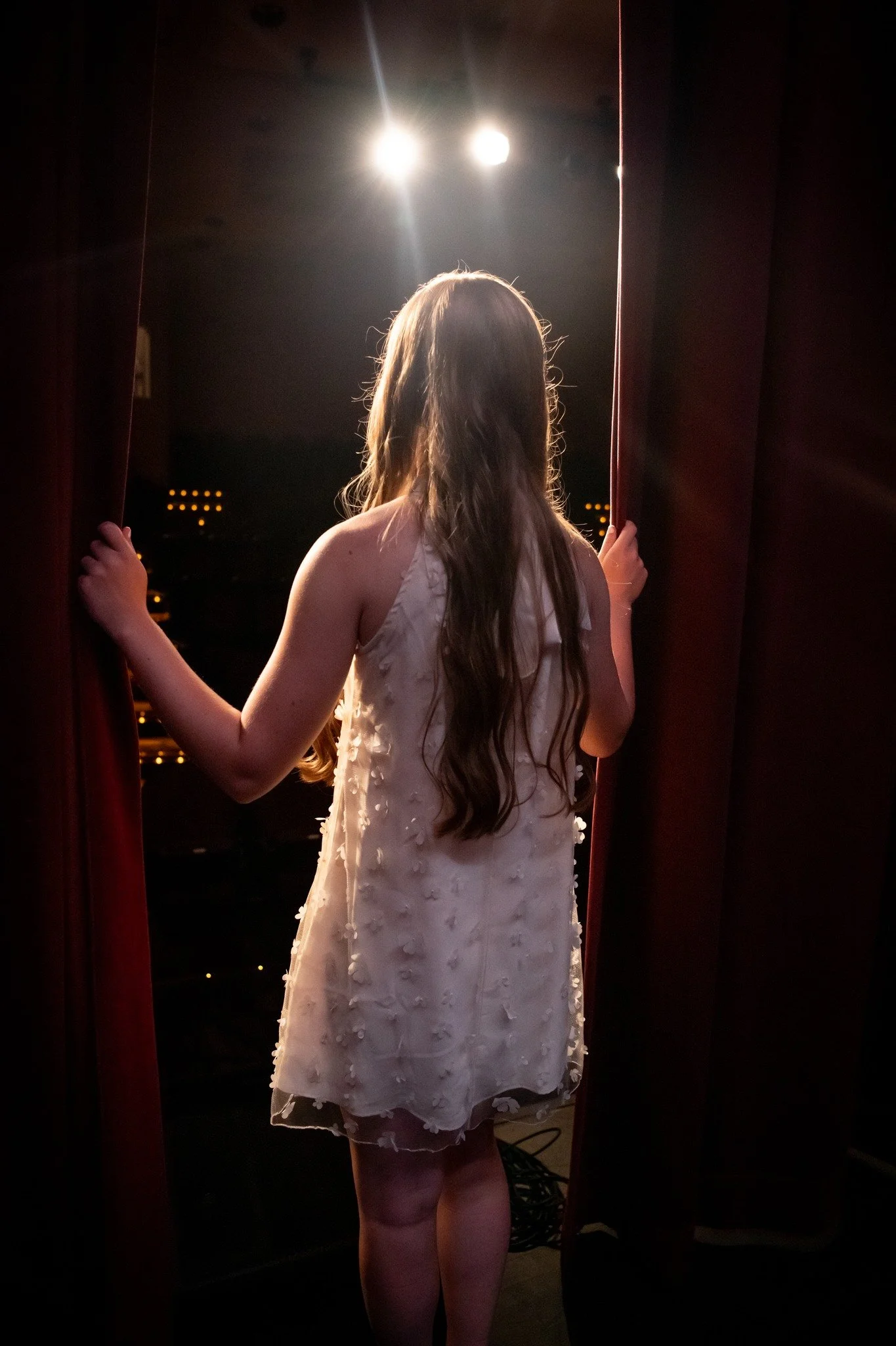 A woman with long hair in a sleeveless dress looking out a window at night.