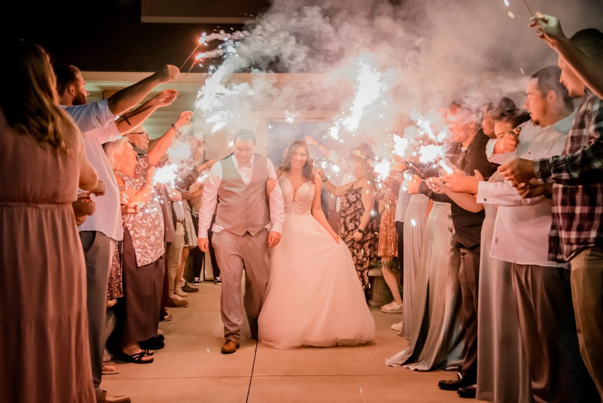 Bride and groom walking through a line of guests holding sparklers at night.