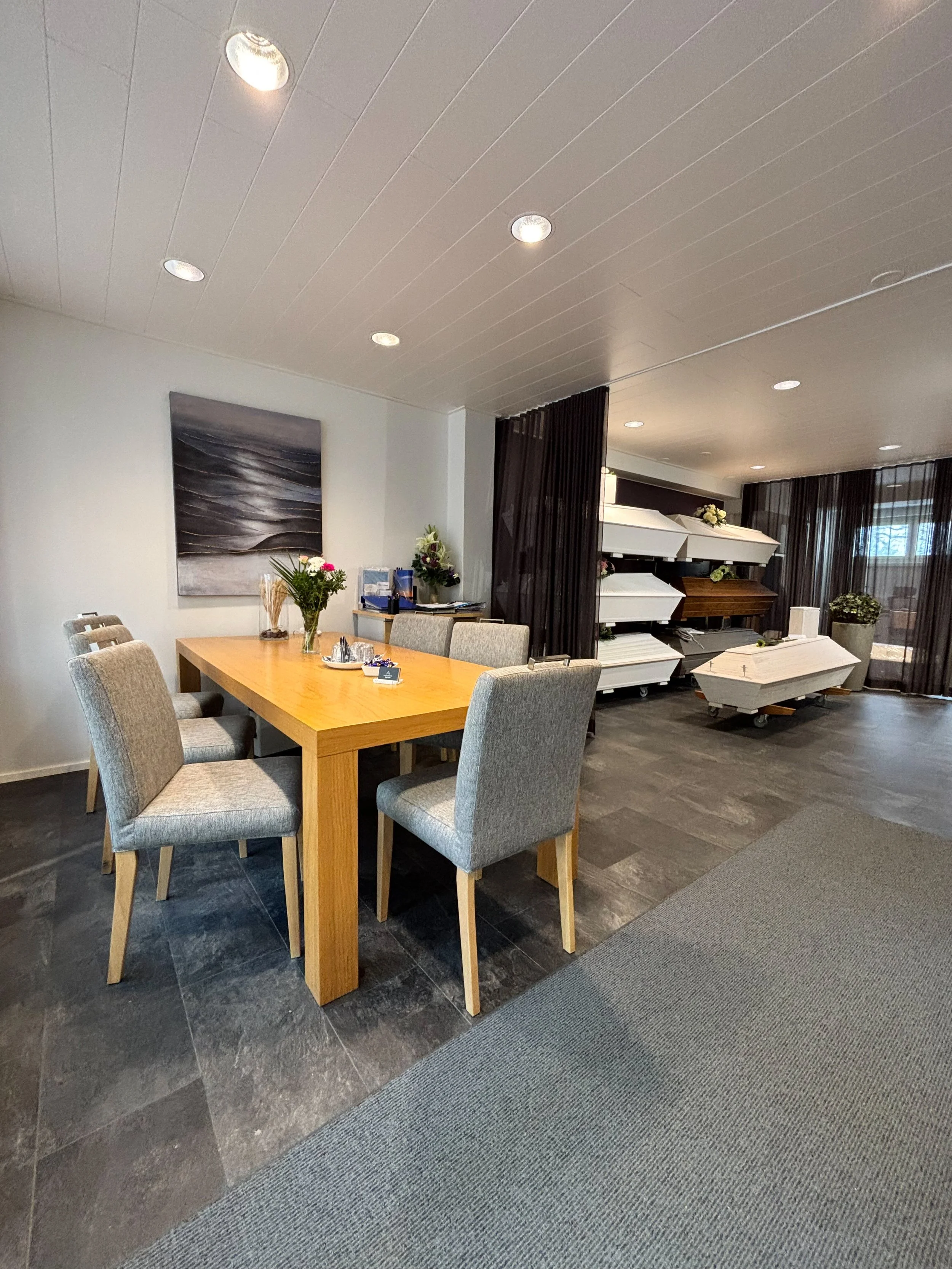 Kuva huoneesta, jossa on ruokapöytä ja tuoleja, sekä reliikejä ja kukkaruukkuja kynttilöineen.