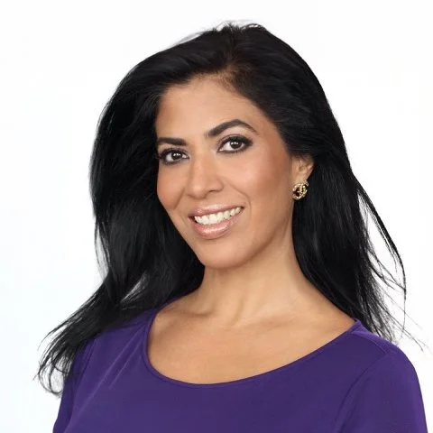 A woman with long black hair wearing a purple top and gold earrings, smiling at the camera.