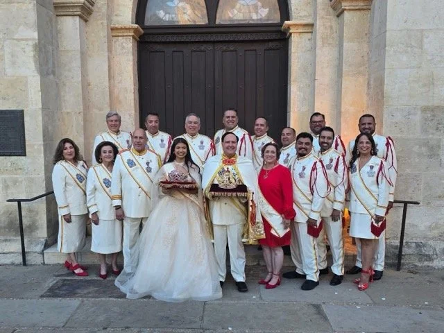 A group of people dressed in formal white and red garments, standing in front of a large wooden door on an ornate building, celebrating a special event.