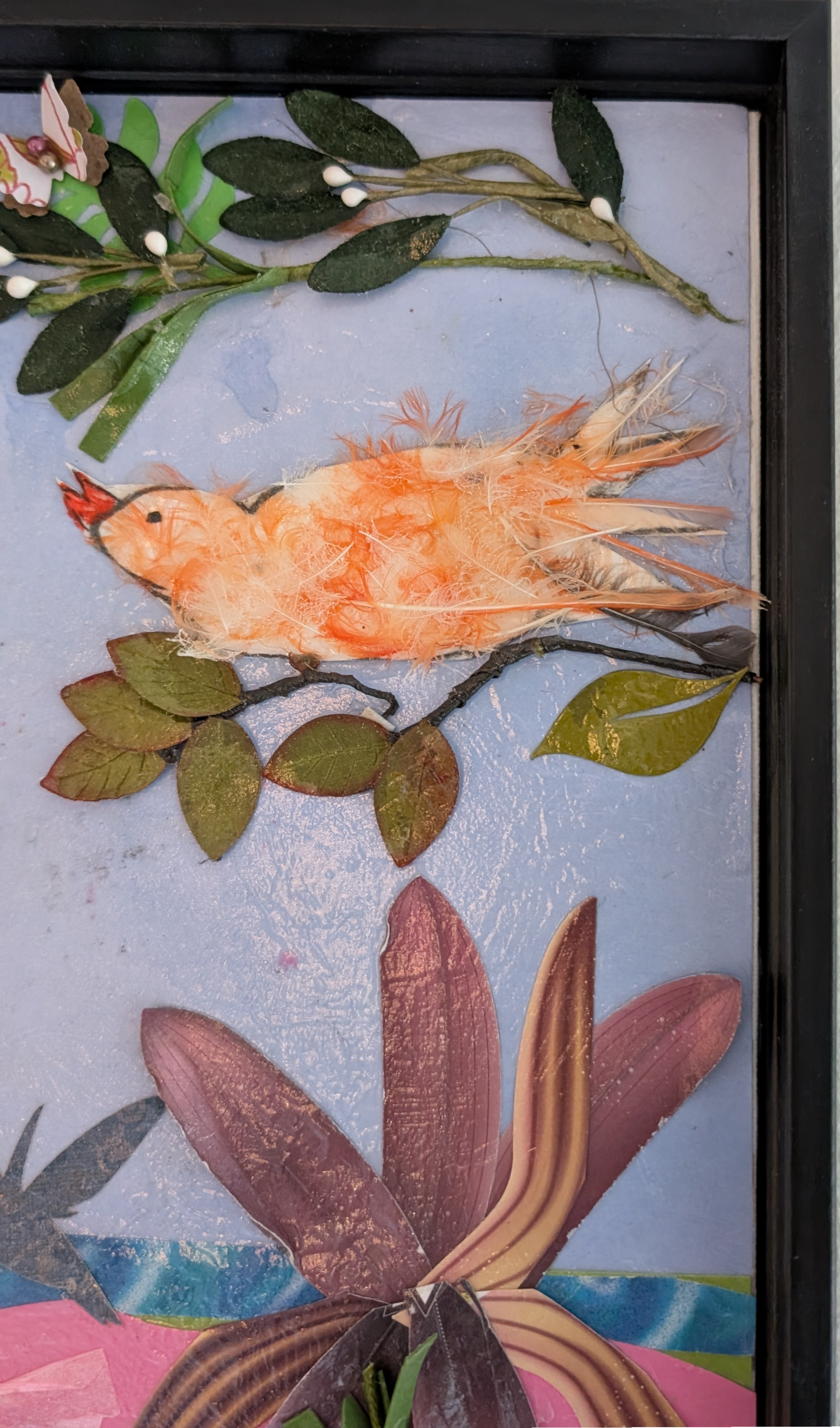 Close-up of orange canary figure built from real canary feathers perched on paper and fabric branch, mixed-media collage by Debra Rich