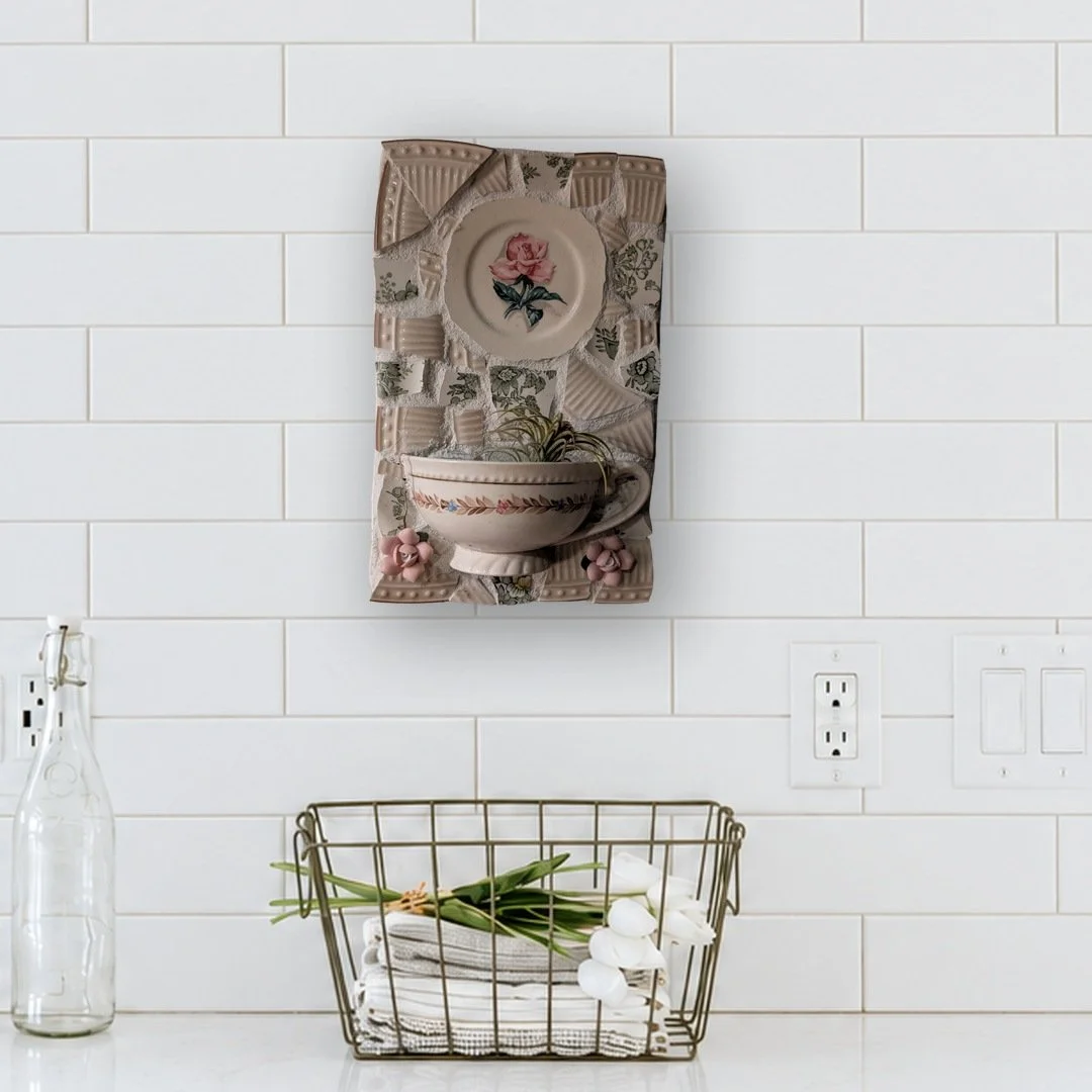 Mosaic wall art with a rose plate and a cup holding an air plant, hung on a white subway tile kitchen wall