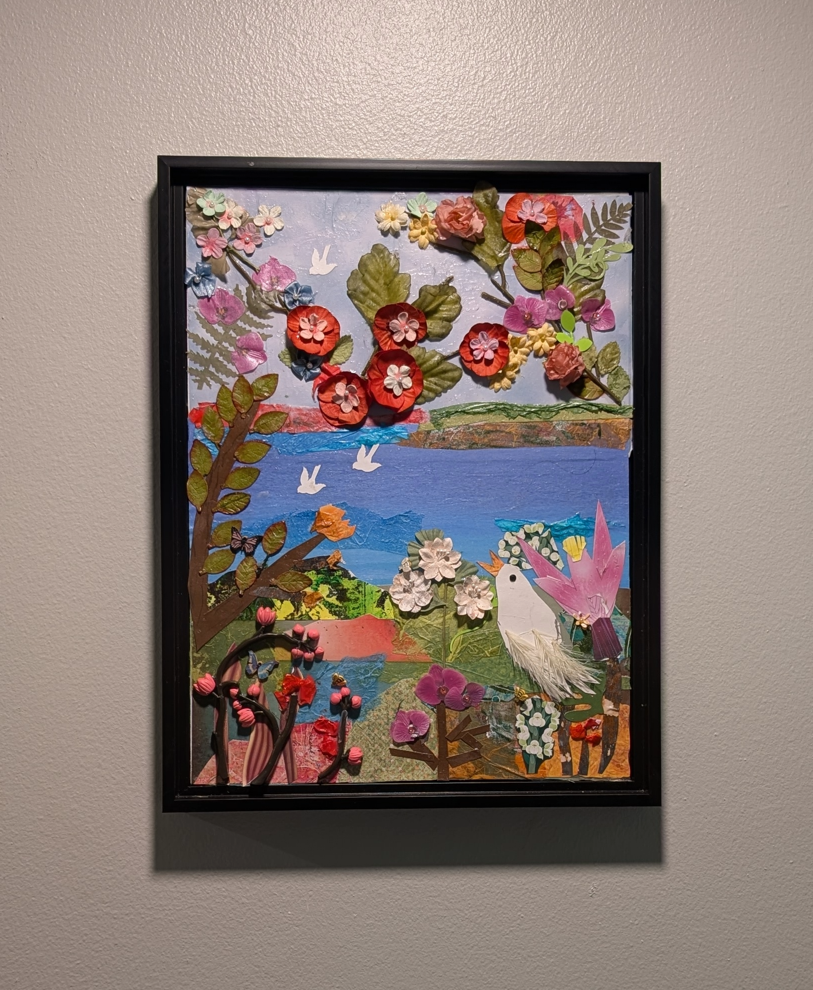 Textured mixed-media collage depicting a vibrant landscape with bright 3D paper flowers, water, & flying white birds on wall, by Sarasota Artist Debra Rich.