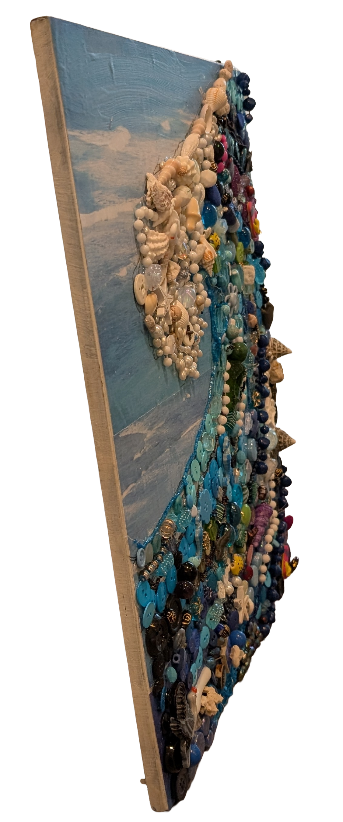 Left side profile view of Waves of Shells and Buttons Collage mosaic art by Debbie Rich, showcasing the 3D depth, layered textures, and raised height of the sea shells and buttons on the board.