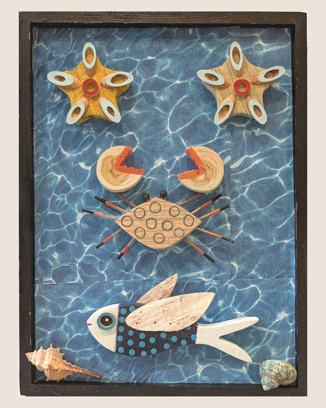 A Fish Tale Assemblage: wooden crab, flying fish and two starfish on water-ripple paper in a black frame