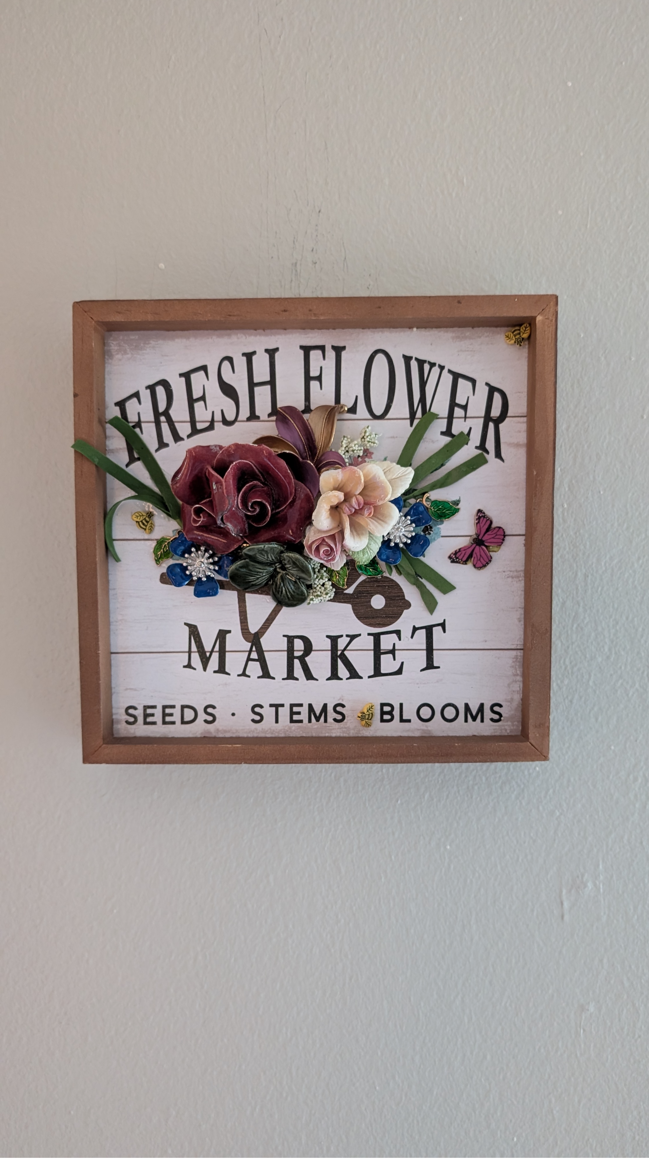 Fresh Flower Market assemblage wall art by Debra Rich displayed on wall — 8x8 shadow box with 3D ceramic flowers, wooden butterfly and gold bees