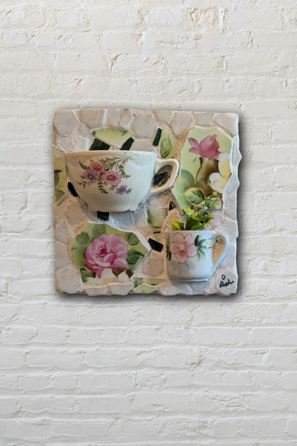 Cups of Joy mosaic wall art hanging on white brick wall — handmade broken china and teacup art by Sarasota artist Debra Rich