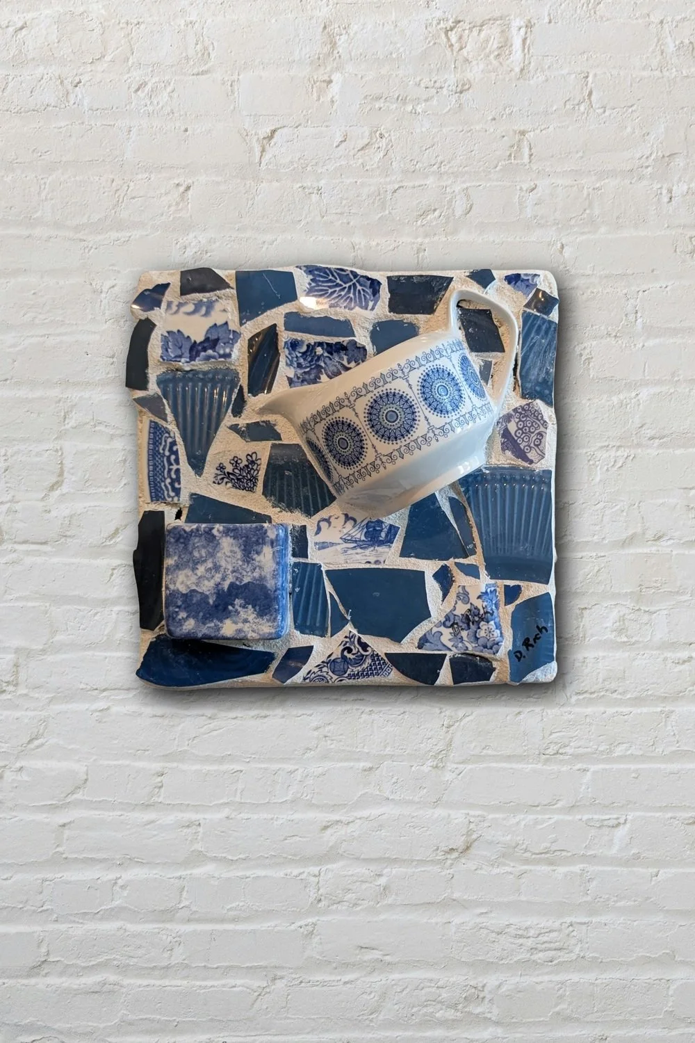 Blue mosaic cup wall art on white brick — handmade broken china mosaic by Sarasota artist Debra Rich