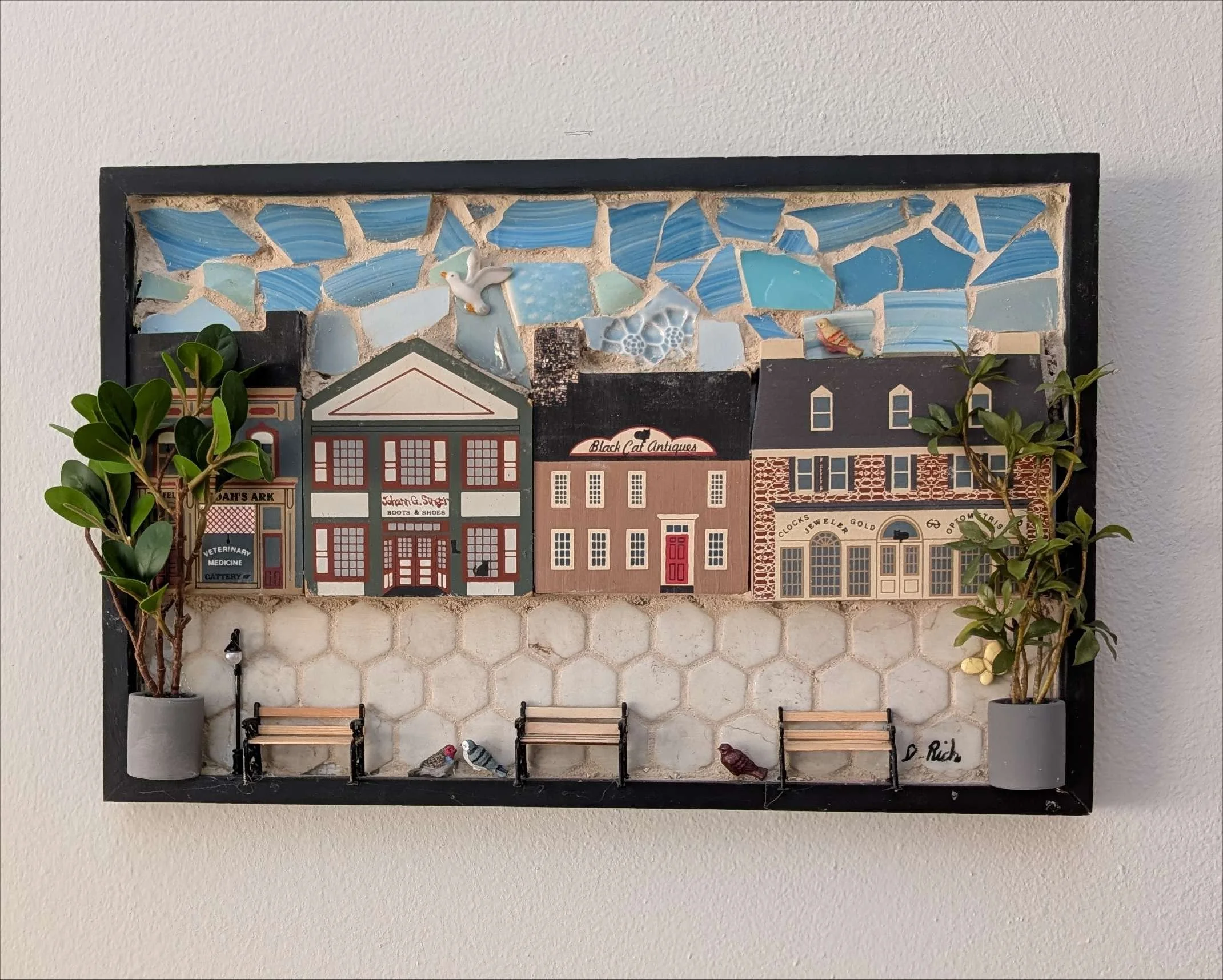 Handcrafted mosaic depicting a charming rustic country village with storefronts and cobblestone path - on a Wall