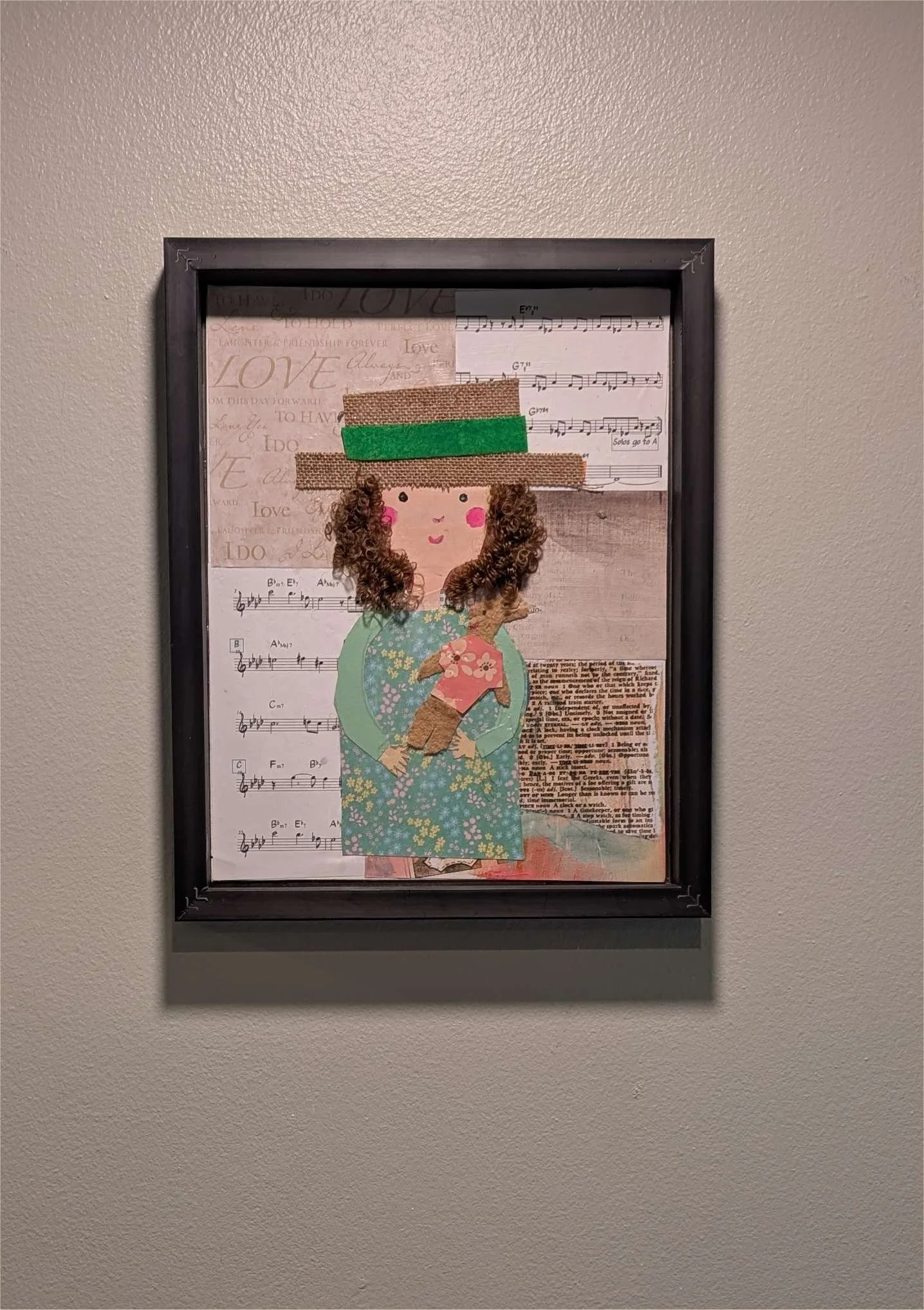 Textured mixed-media collage depicting a young girl with curly hair, with a hat on, holding her stuffed animal surrounded by sheet music on wall, by Sarasota Artist Debra Rich.