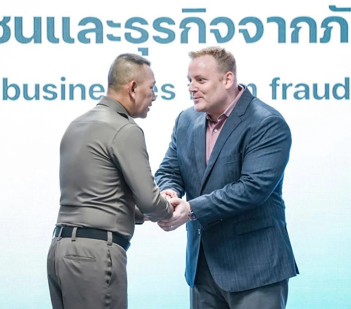 Two men shake hands in a formal setting with a background displaying text about business fraud.