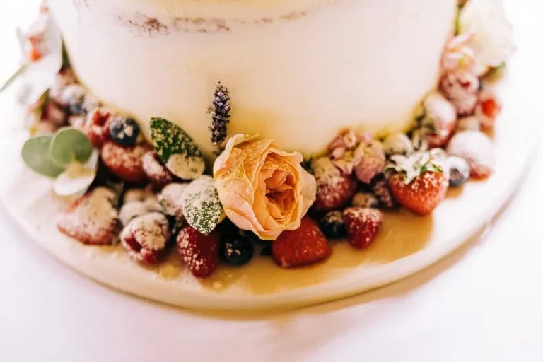 Close-up of a wedding cake decorated with strawberries, blueberries, a peach-colored rose, and greenery.