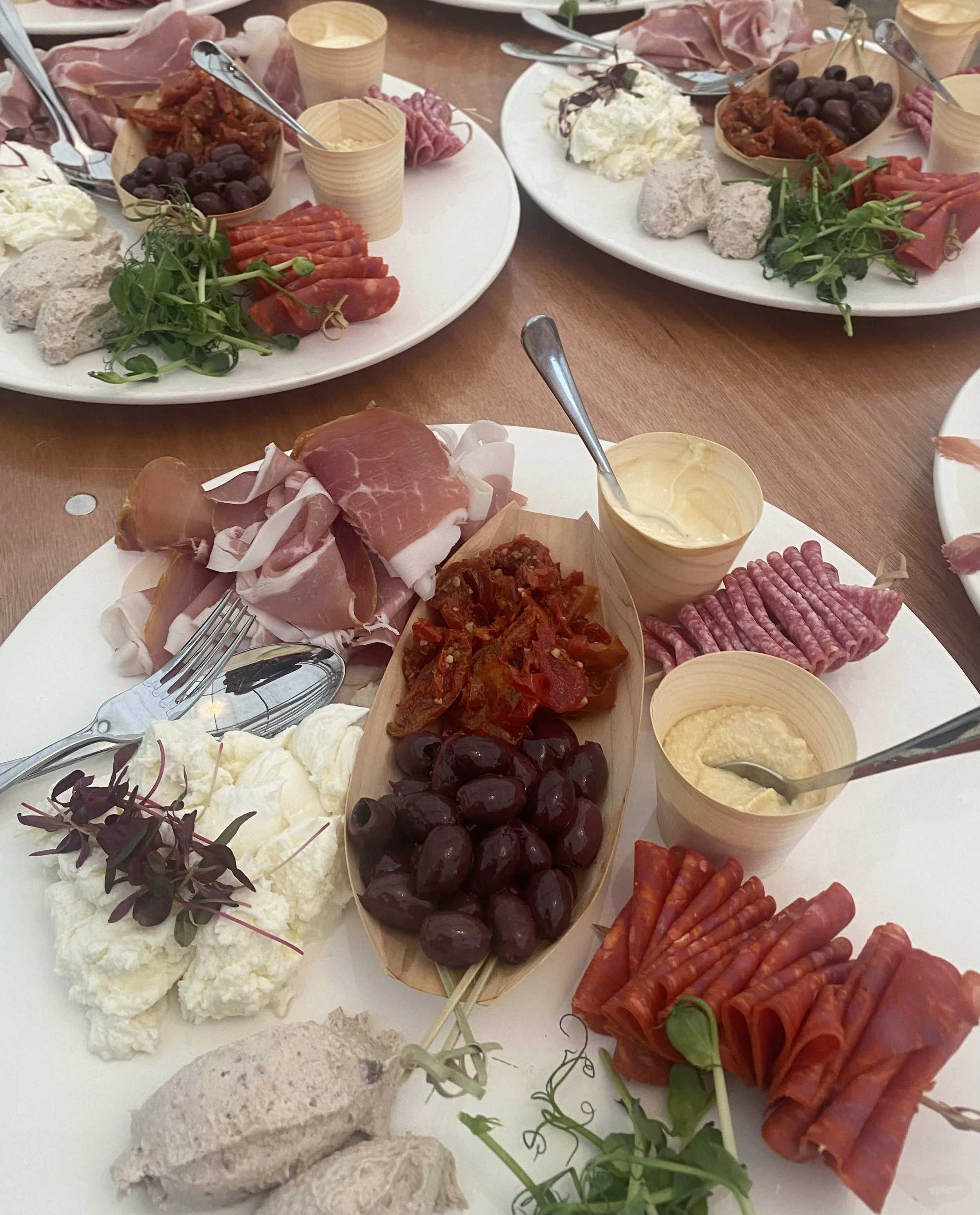 Assorted charcuterie platter with meats, cheeses, grapes, and spreads on a white plate with smaller bowls of dips or spreads.