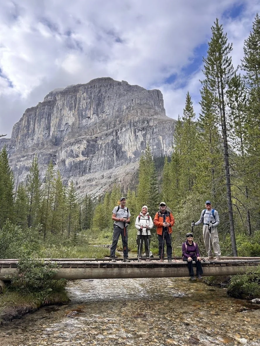 Four hikers on a footbridge below a limestone cliff on the Stanley Glacier trail, Kootenay National Park