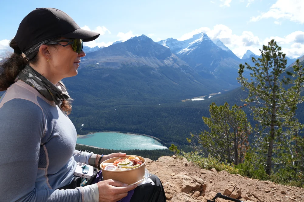 Hiker with a lunch bowl at Paget Lookout above a turquoise lake in Yoho National Park, near Field BC