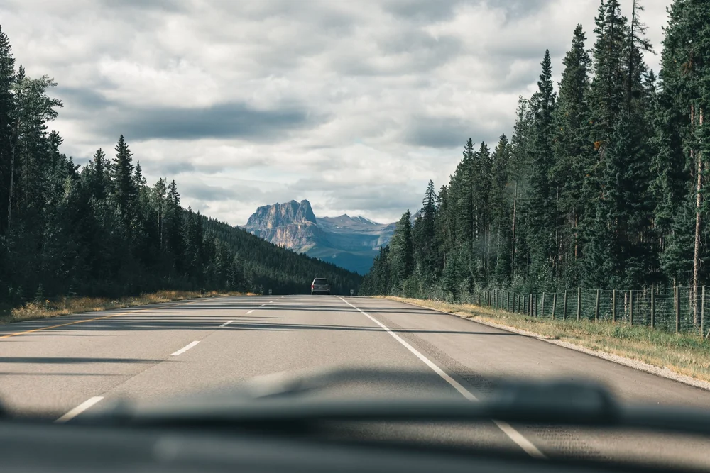 Scenic highway through forest toward Rocky Mountain peaks on the drive to Banff National Park
