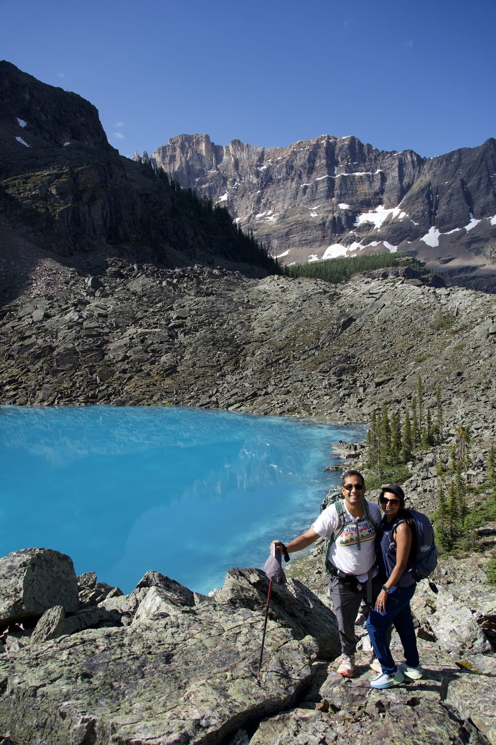 Two hikers beside a turquoise lake below rocky peaks in the Lake O’Hara area, Yoho National Park