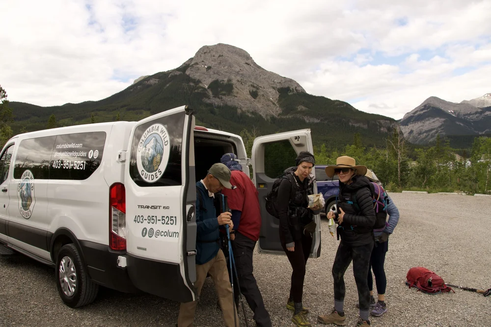 Guests with hiking poles beside the Columbia Wild Guides private transfer van, Canadian Rockies near Banff