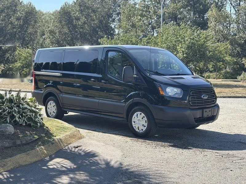 Black Ford Transit passenger van parked outdoors beside trees