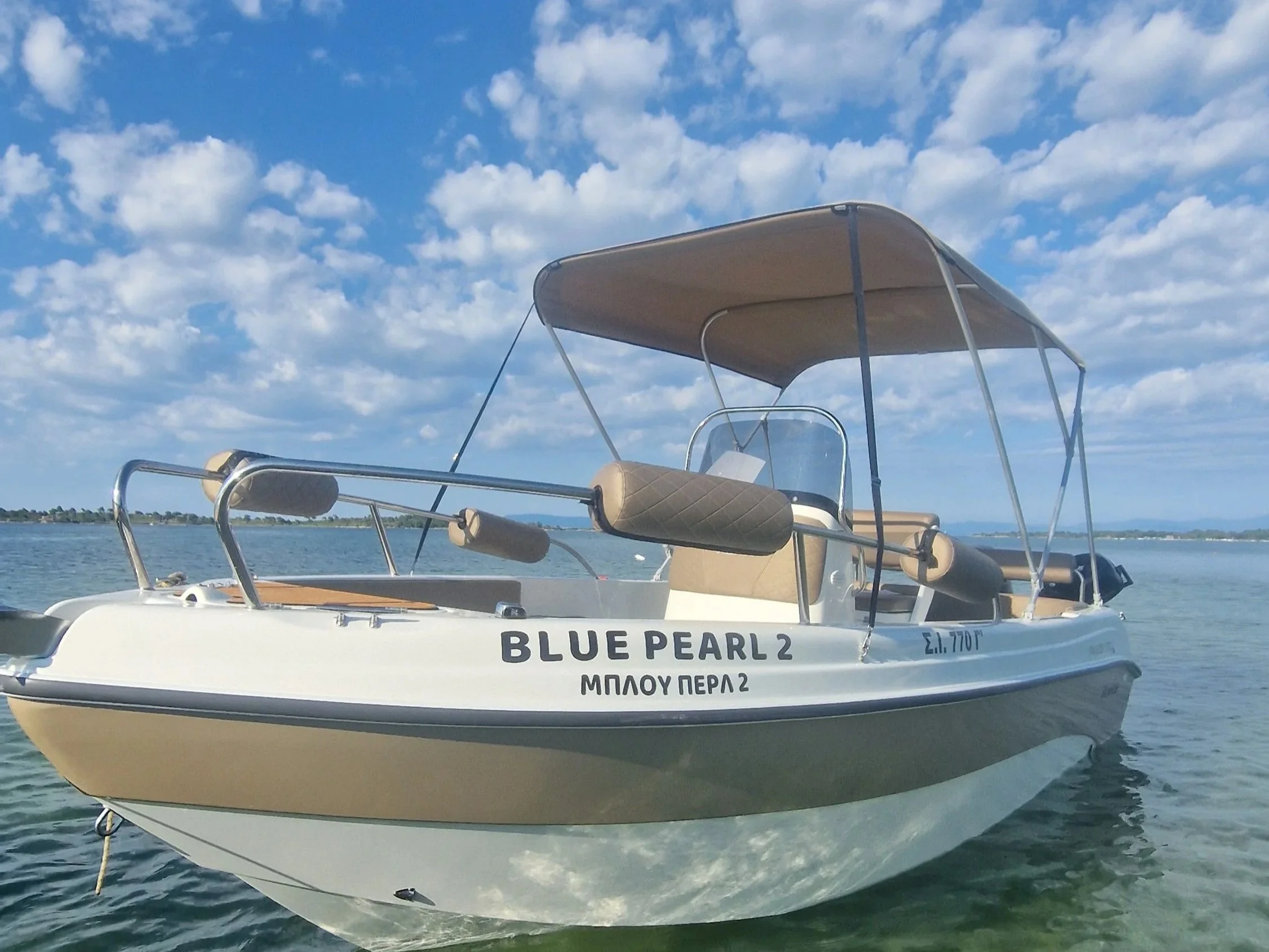A white boat named BLUE PEARL 2 with a beige canopy floating on water under a blue sky with scattered clouds.