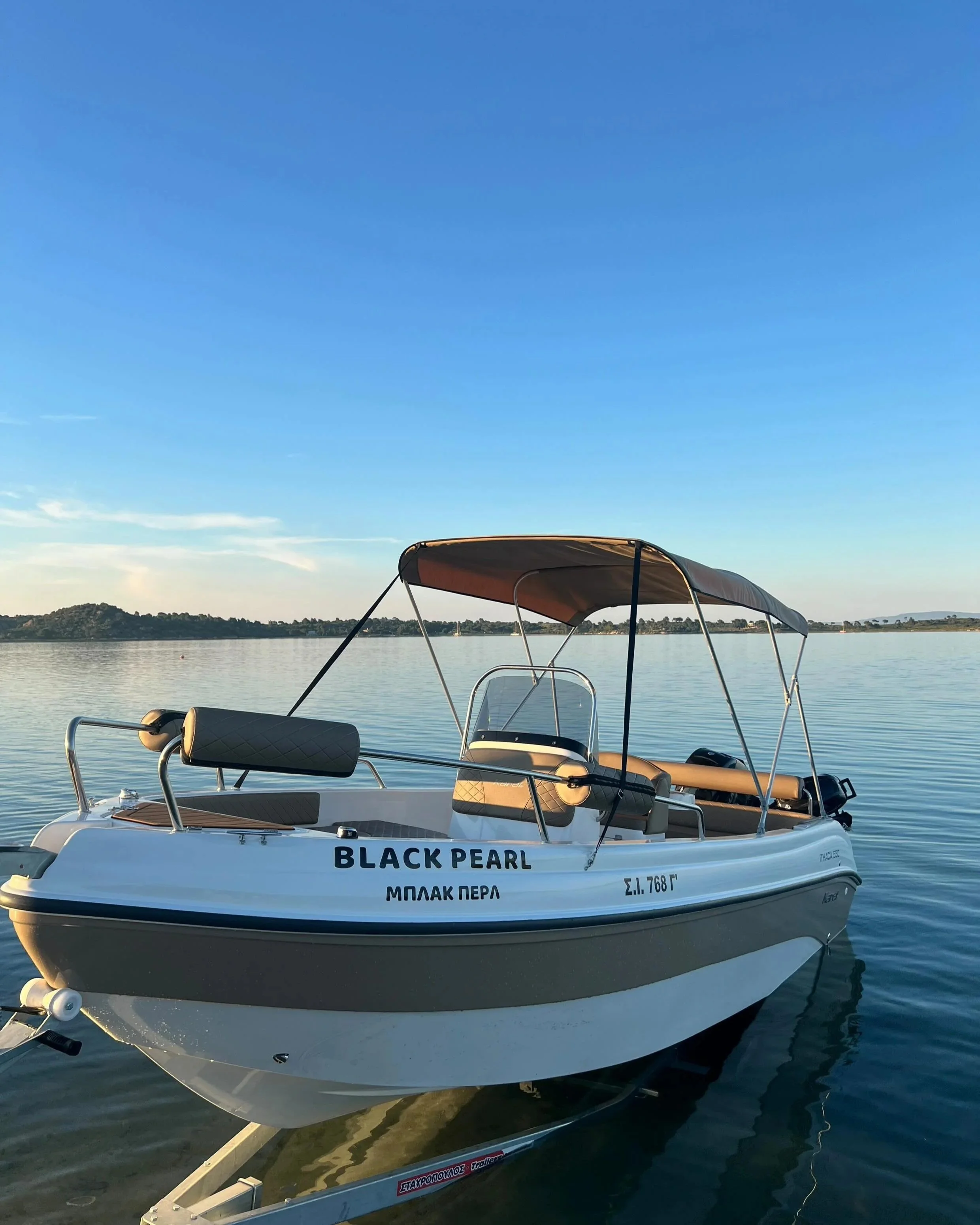 A white speedboat named 'Black Pearl' docked on a calm body of water, with a cityscape and hillside in the distance under a clear blue sky.