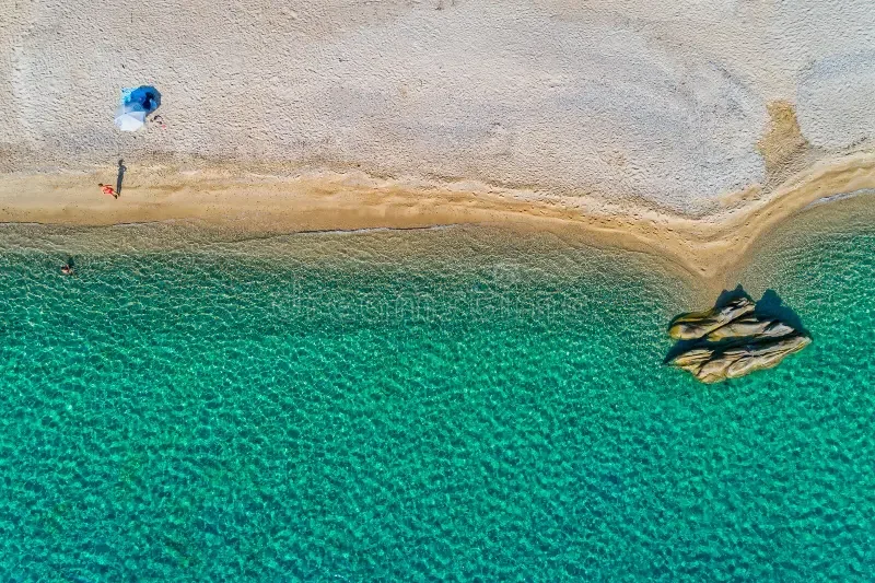 Aerial view of a sandy beach with clear turquoise water, a small tent near the shore, and a boat anchored close to the beach.