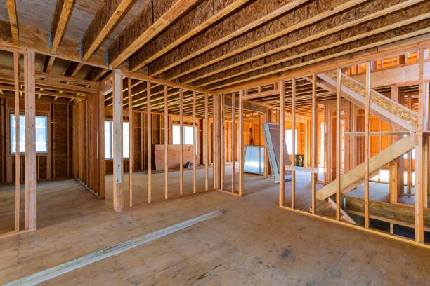 Interior of a house under construction showing exposed wooden framing, staircase, and several windows.