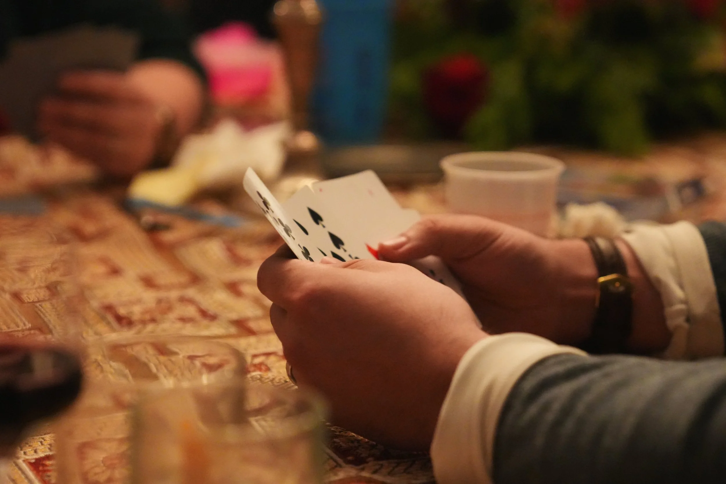 A person holding a hand of playing cards, dealing or playing a game at a table with a patterned tablecloth.