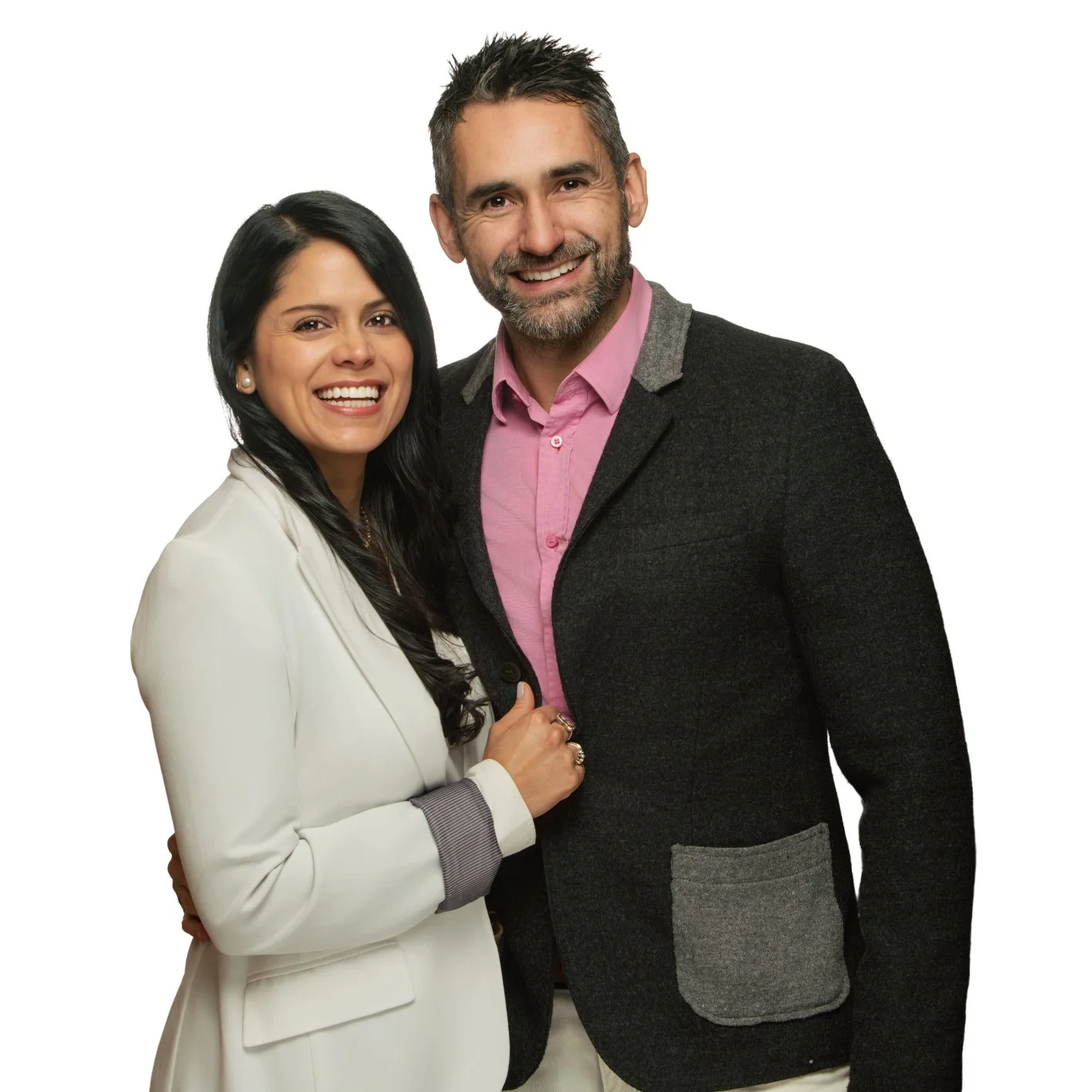 Smiling man and woman standing closely together against a white background, the woman wearing a white blazer and the man in a dark blazer with pink shirt.